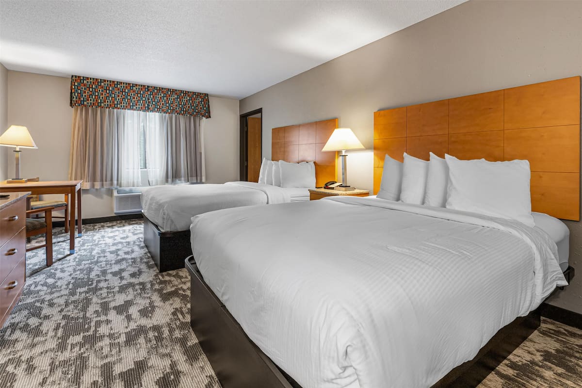 A hotel room with two beds, a desk, and a chair.