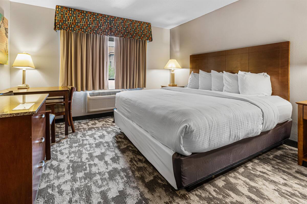 A hotel room with a large bed, two bedside tables, a desk, and an air conditioning unit.