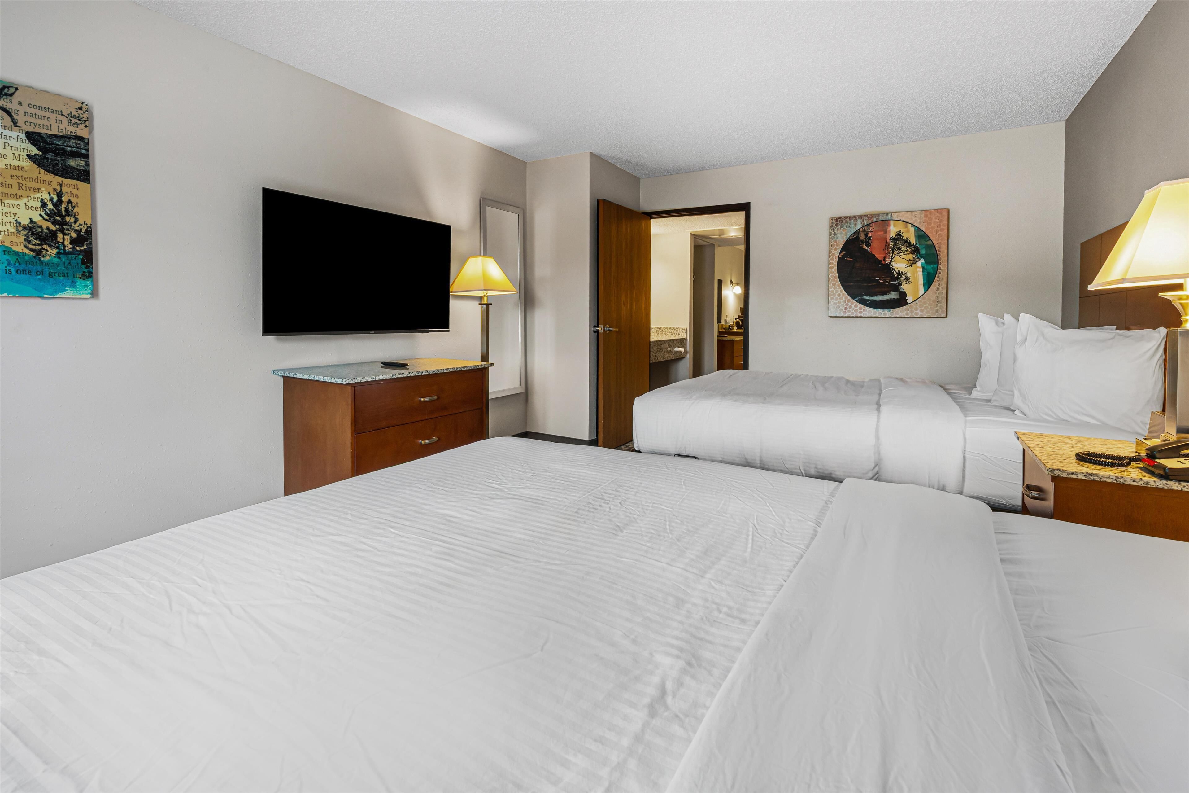 A hotel room with two beds, a flat-screen TV, a wooden dresser, and a painting on the wall.