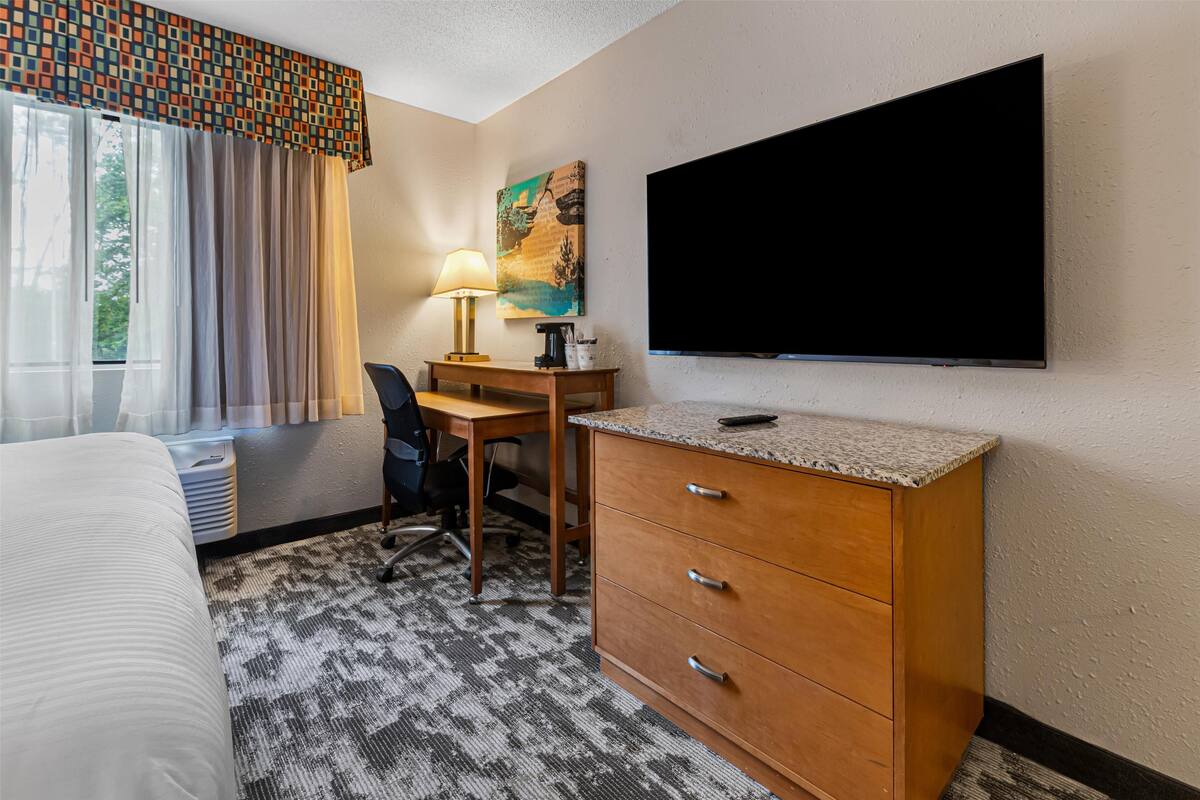 A hotel room with a bed, a desk with a lamp, a TV, and a painting on the wall.
