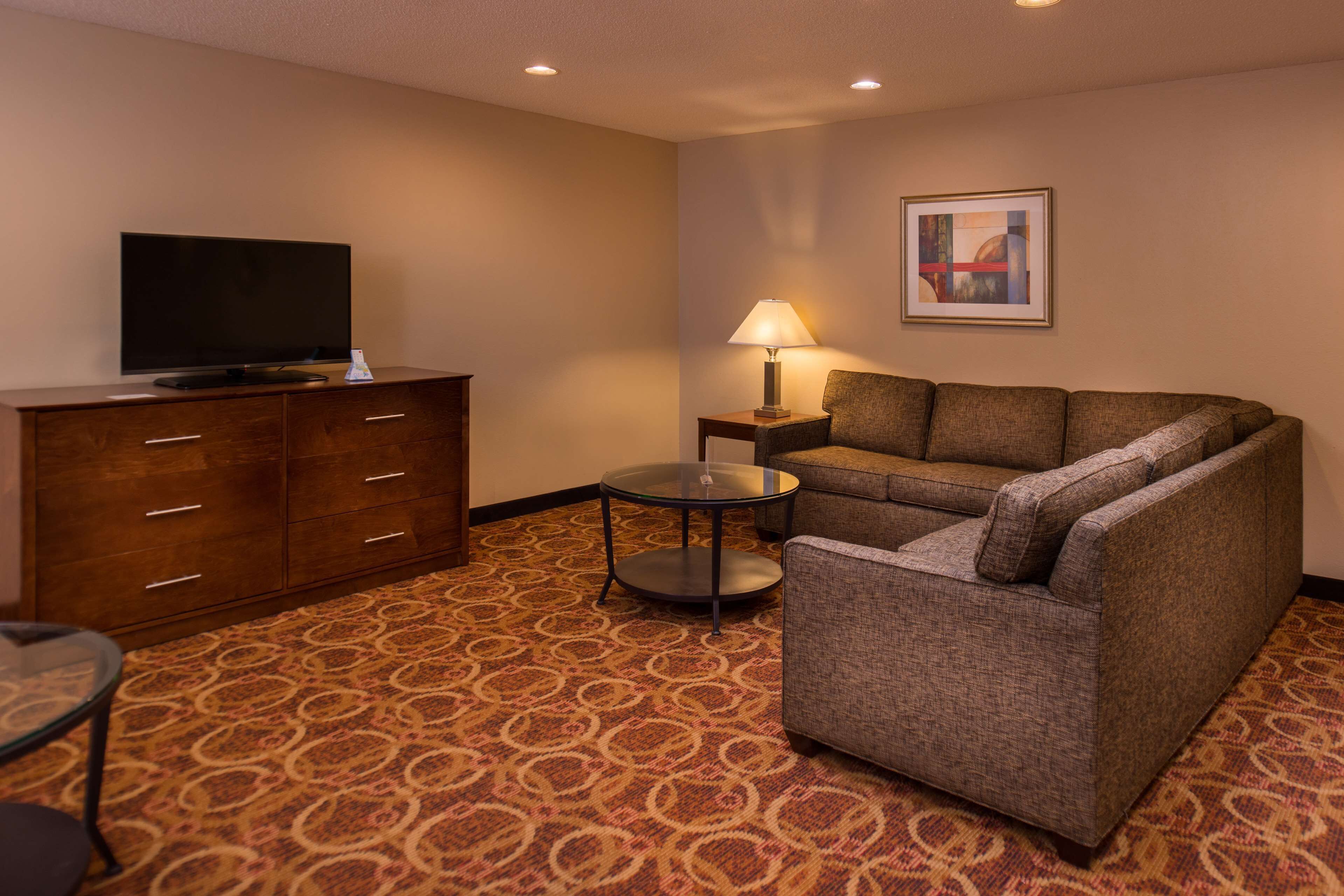 A hotel room with a sofa, a television on a wooden cabinet, a lamp on a side table, and a patterned carpet.