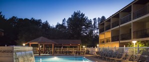 A pool area with lounge chairs, a covered seating area, and a building with balconies.