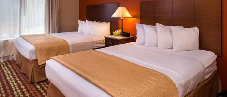 A hotel room with two beds, a nightstand with a lamp, and a patterned carpet.