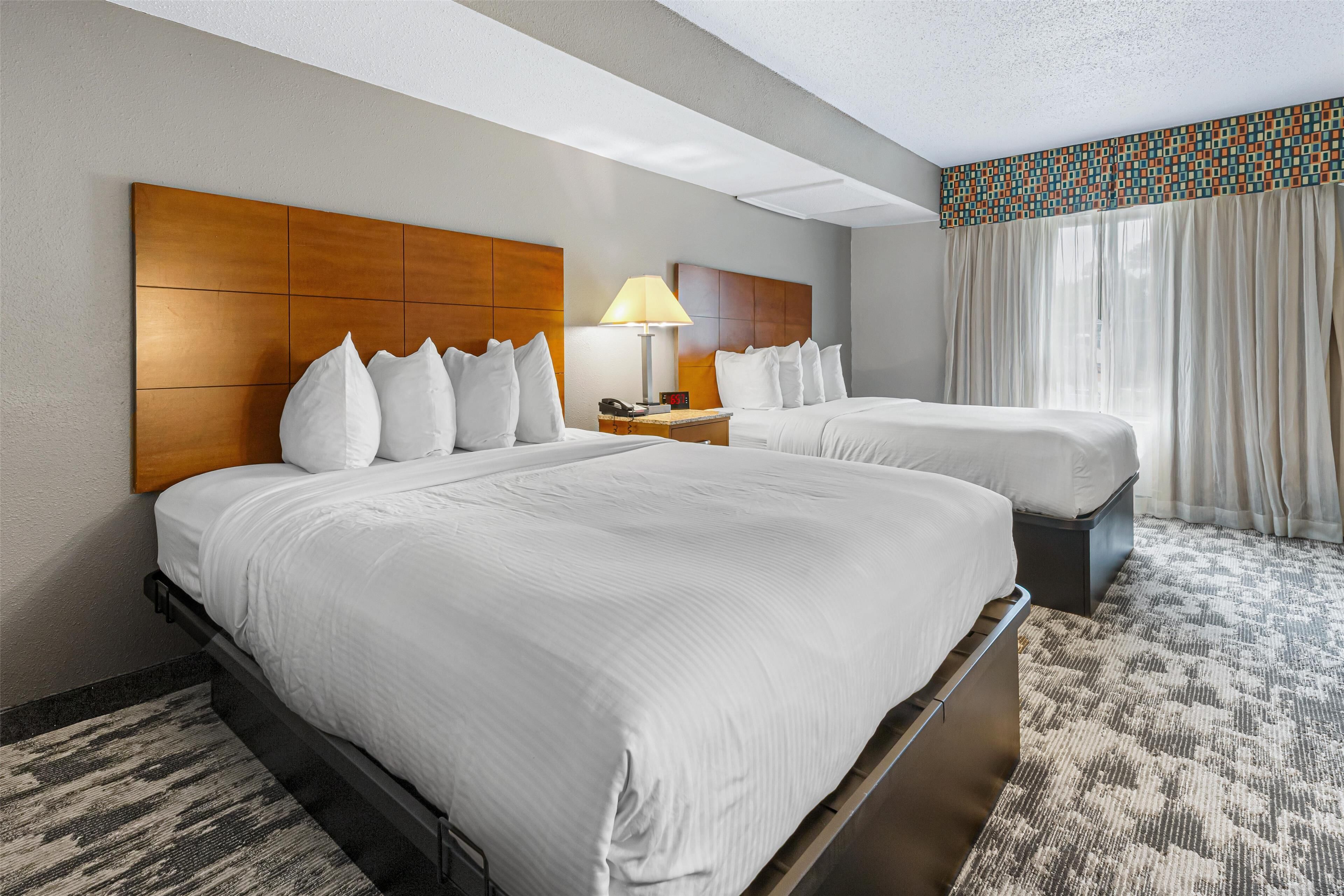 A hotel room with two beds, a nightstand with a lamp, and a window with curtains.