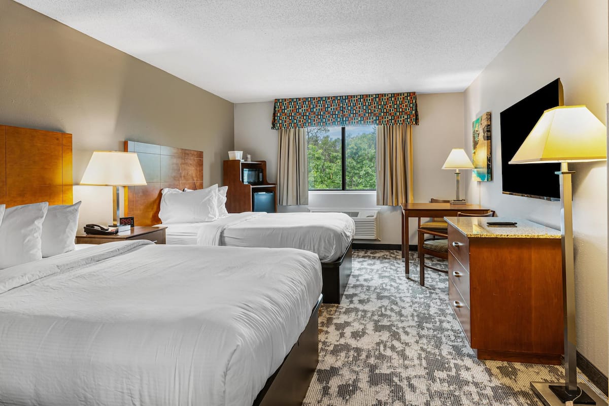 A hotel room with two beds, a desk, a chair, a television, and a window with curtains.