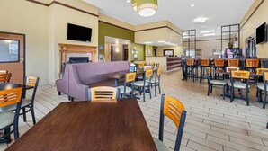 A hotel lobby with a wooden reception desk, a purple sofa, multiple dining tables with chairs, and a fireplace. - Best Western Ambassador Inn & Suites (Wisconsin Dells)