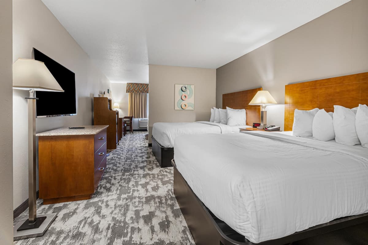 A hotel room with two beds, a desk, a chair, a TV, and a wall-mounted artwork.