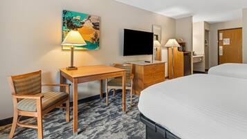 A hotel room with a bed, a desk with a chair, a television, a desk lamp, a wooden dresser, and a painting on the wall.