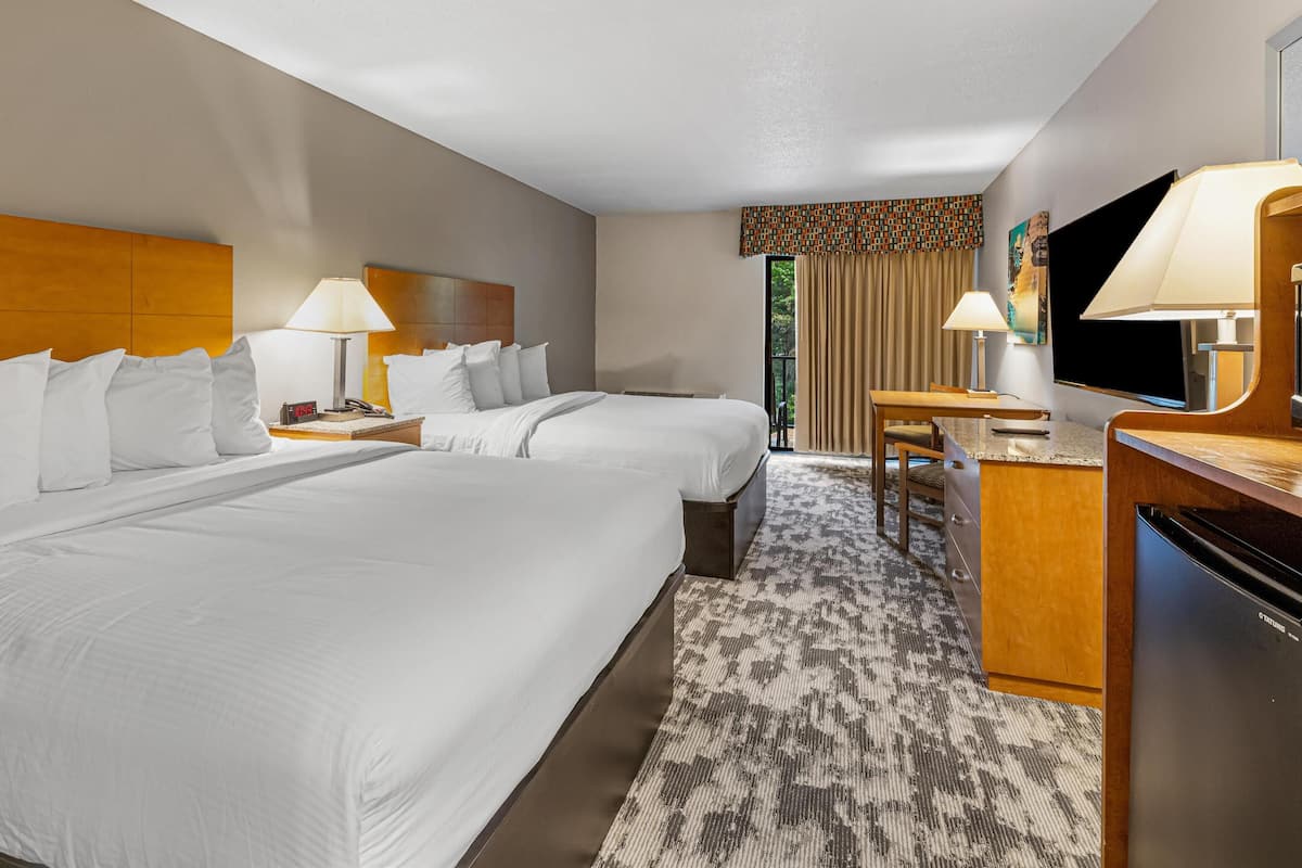 A hotel room with two beds, a desk, a television, and a refrigerator.