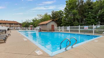A swimming pool with a white fence, a small building, and lounge chairs.