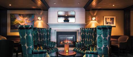 A cozy lounge area with two green upholstered armchairs, a small round table, and a fireplace.