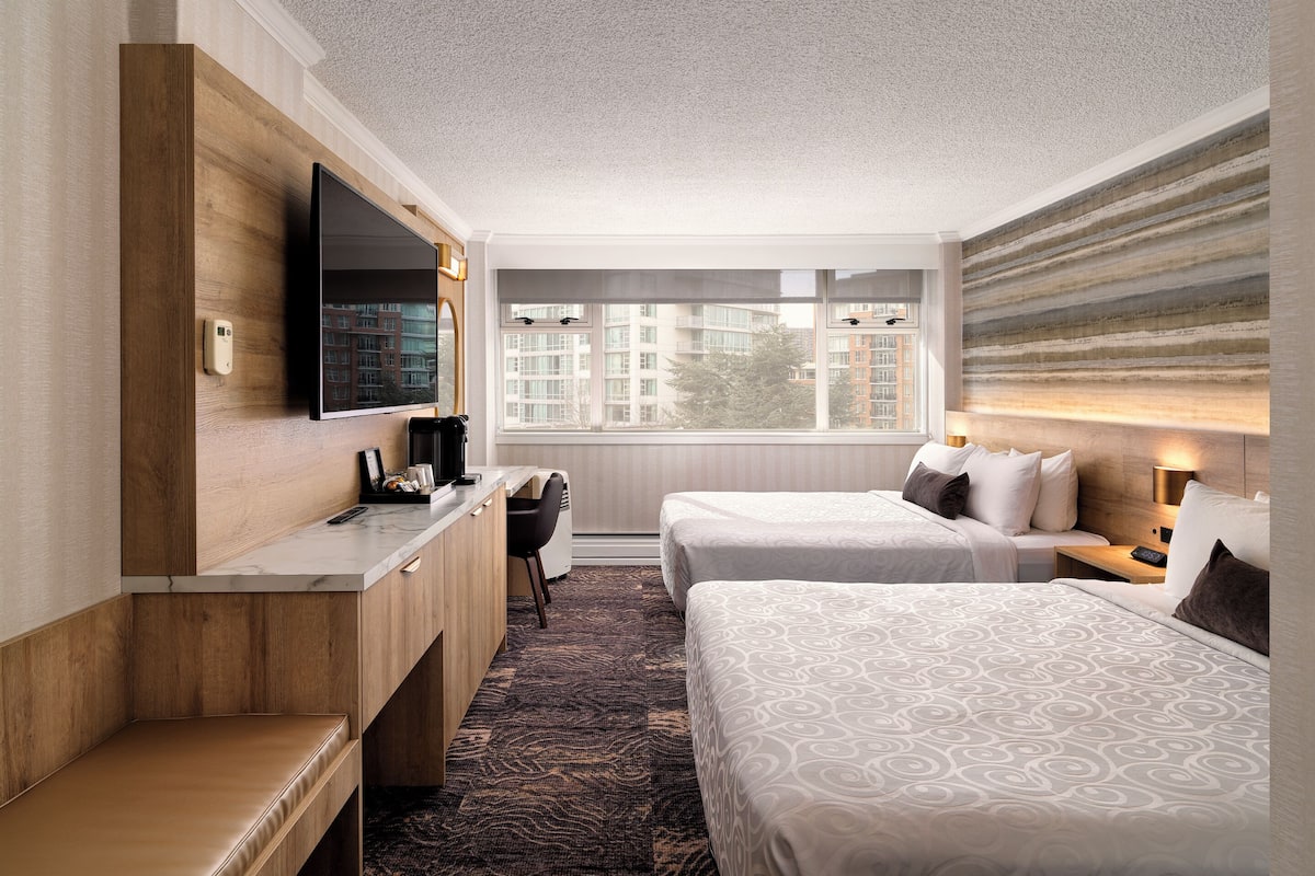 A hotel room with a bed, a desk, a chair, a TV, and a window with a view of buildings.