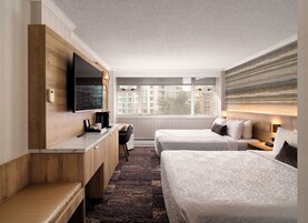 Habitación de hotel con cama, escritorio, silla, televisión y ventana con vistas a edificios.