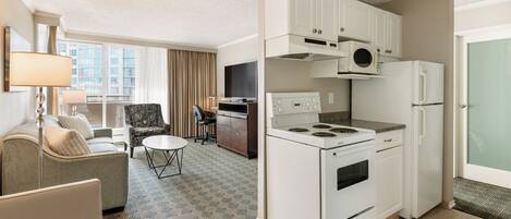 Habitación de hotel compacta con kitchenette, sofá, mesa de comedor y vistas a la ciudad.