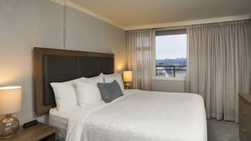 A hotel room with a large bed, a nightstand with a lamp, a bedside table with a vase, and a view of the city through the window.