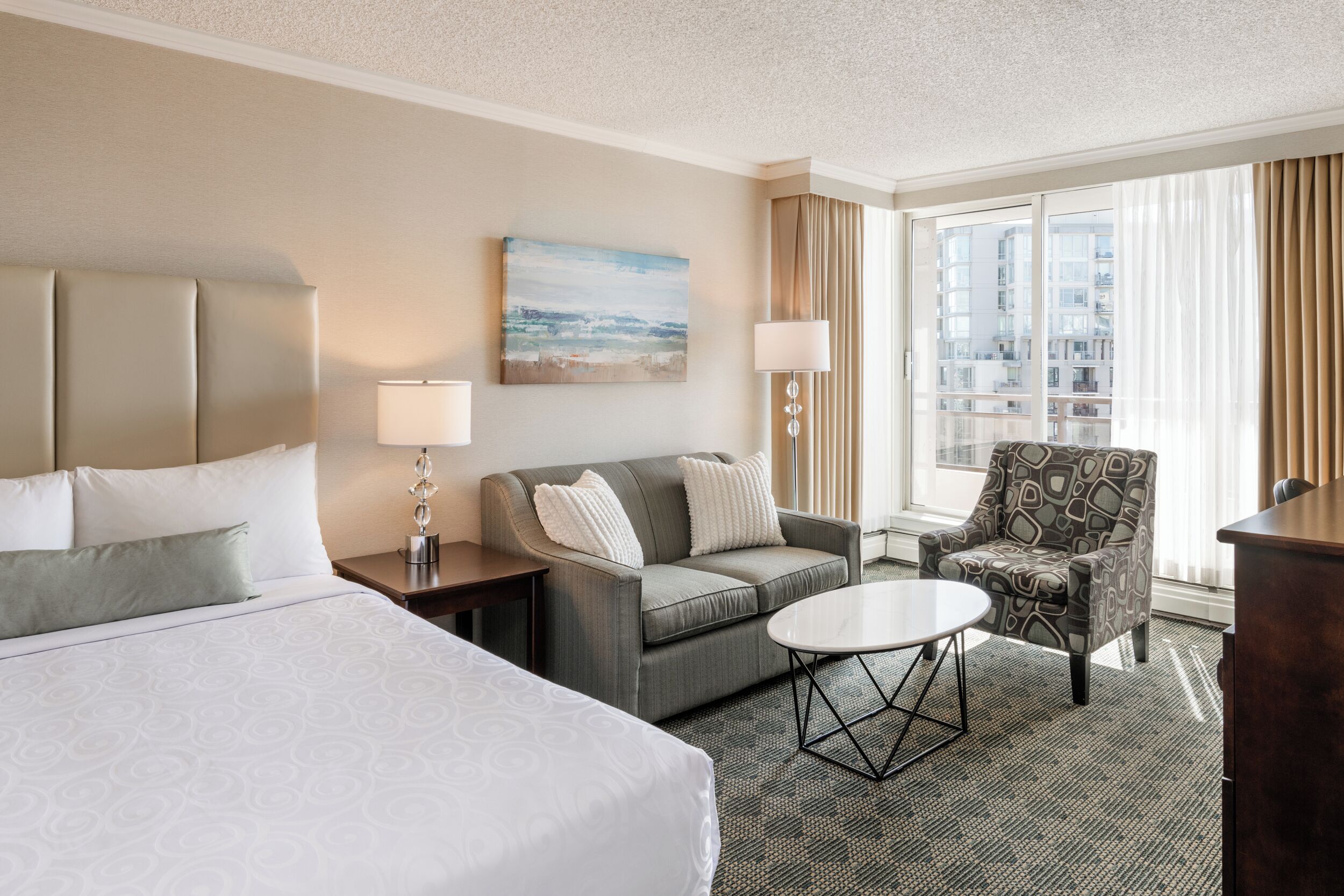 Une chambre d’hôtel avec un lit, un canapé, une chaise, une petite table et un tableau au mur.