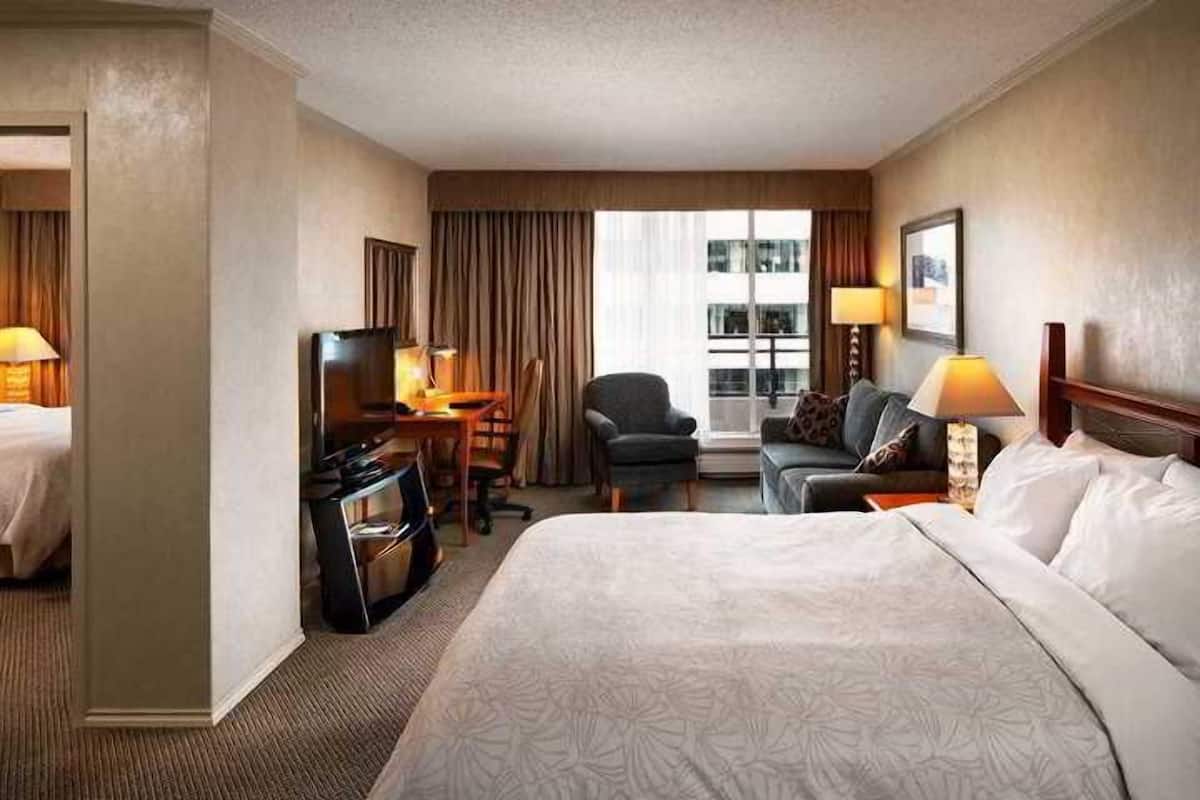 A hotel room with a large bed, a desk with a computer, a TV, and a seating area with a couch and chairs.