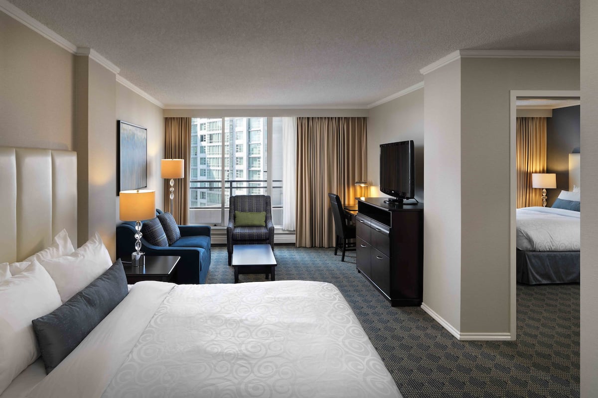 A hotel room with a large bed, a desk with a TV, a chair, and a view of a cityscape through the window.