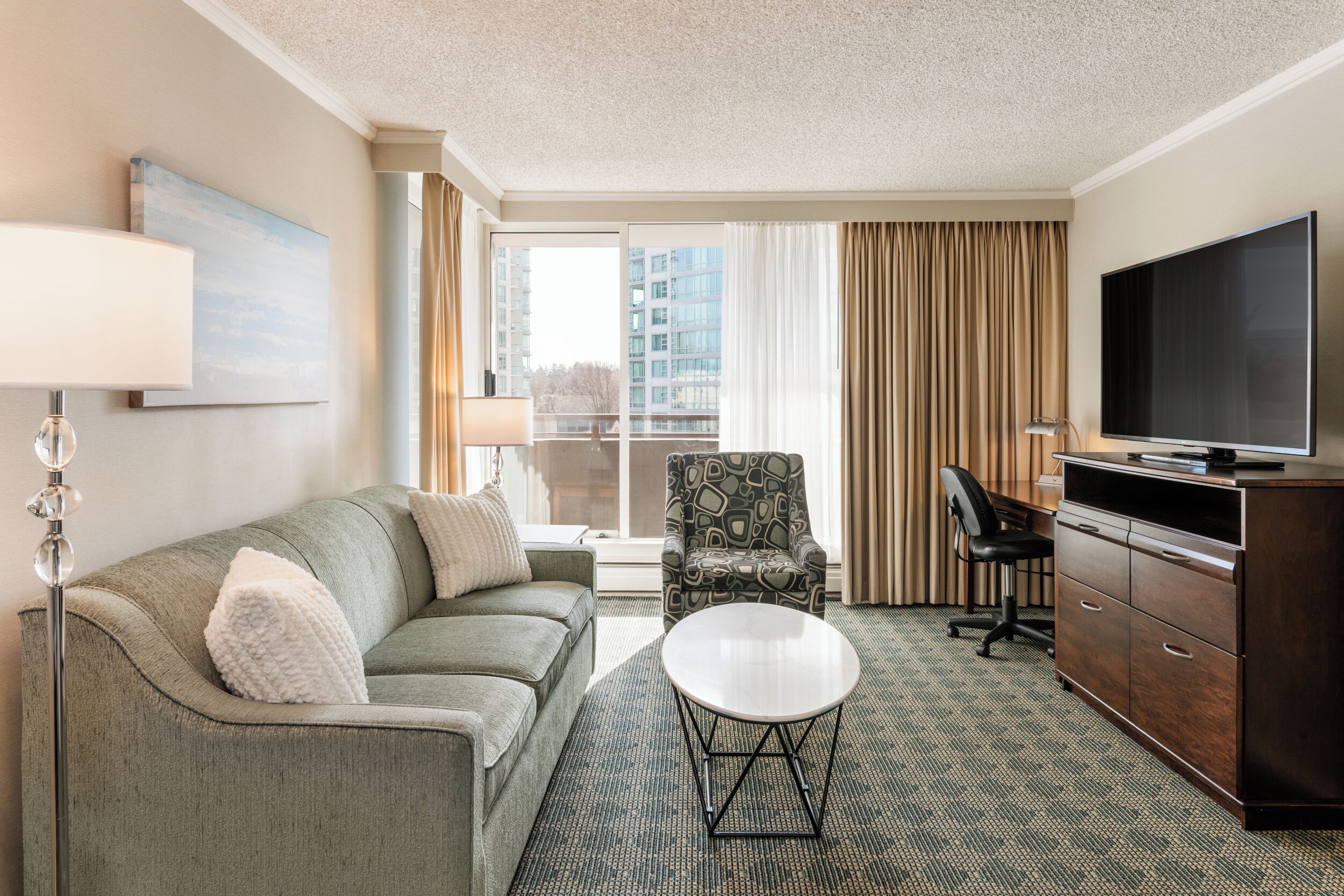 A hotel room with a sofa, armchair, TV, and a desk with a chair.
