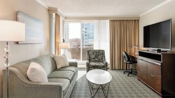 Ein Hotelzimmer mit Sofa, Sessel, Fernseher und Schreibtisch mit Stuhl.