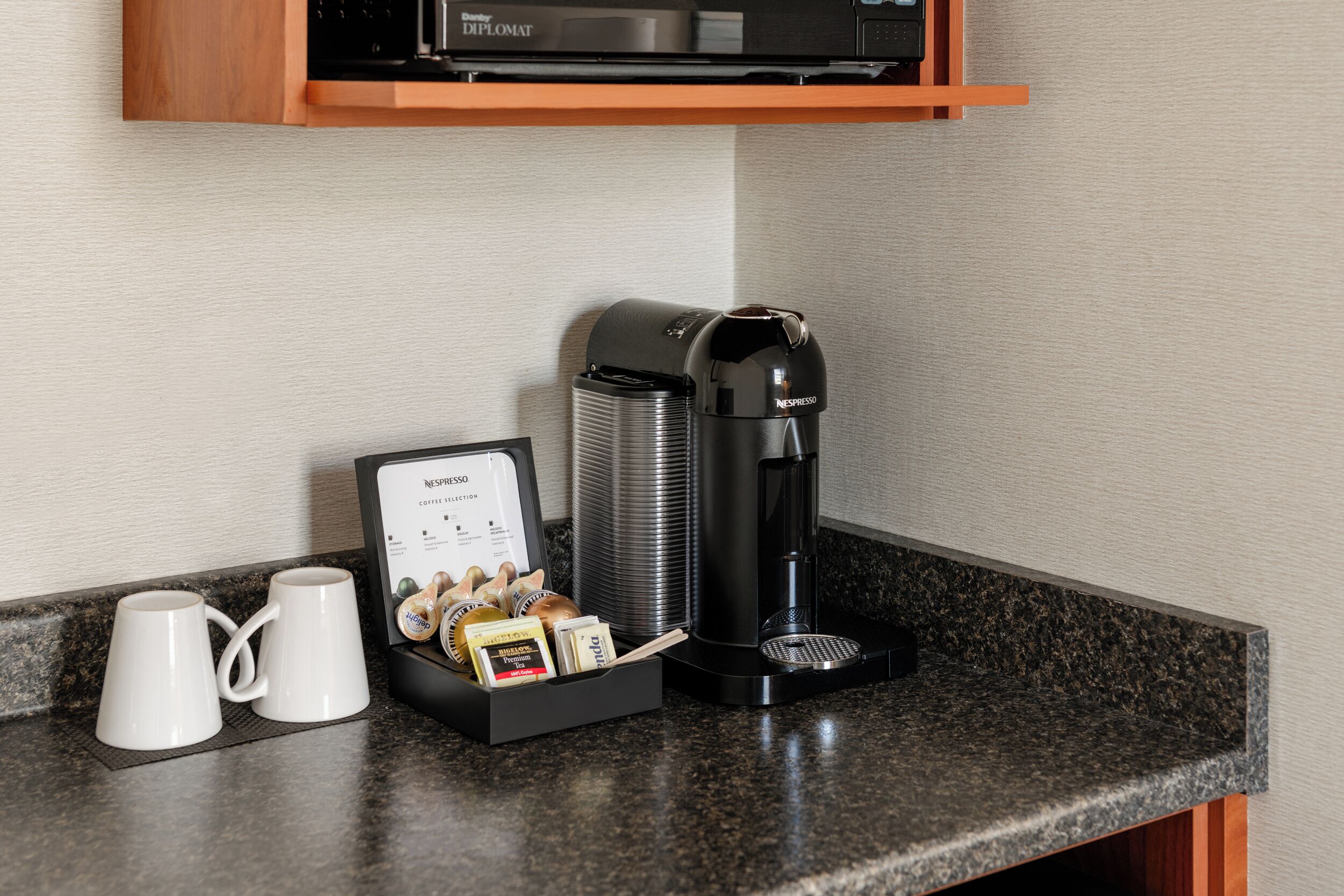 A coffee machine with a coffee pod holder and two white mugs on a countertop.