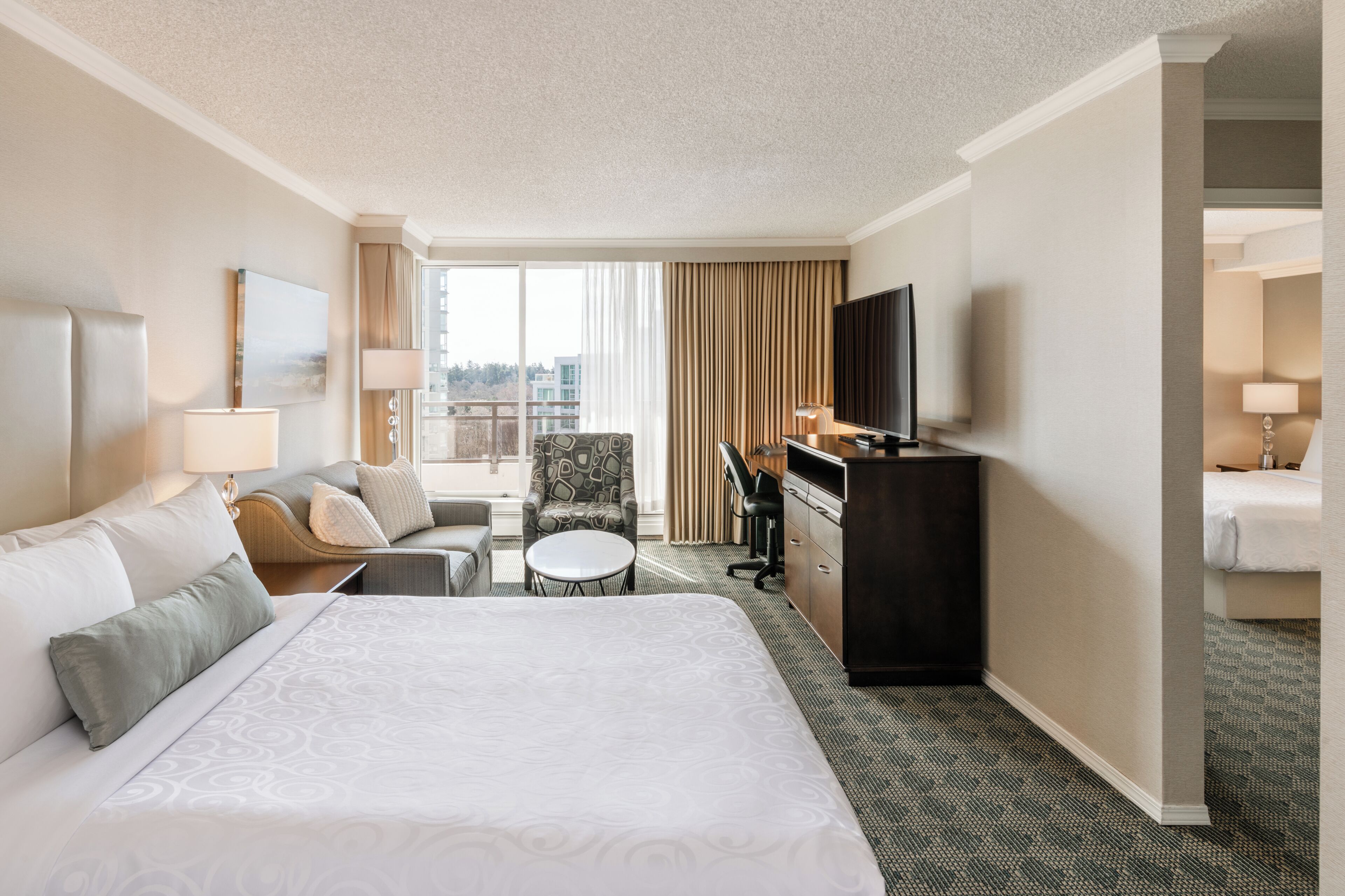 Une chambre d’hôtel avec un grand lit, un bureau, une chaise, une télévision et une vue sur la ville par la fenêtre.