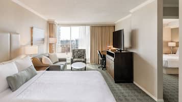 A hotel room with a large bed, a desk, a chair, a television, and a view of the city through the window.