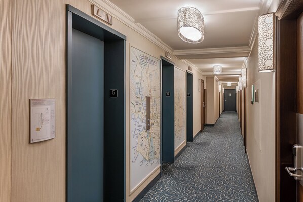Un pasillo de hotel con puertas numeradas, un mapa en la pared y alfombra estampada.