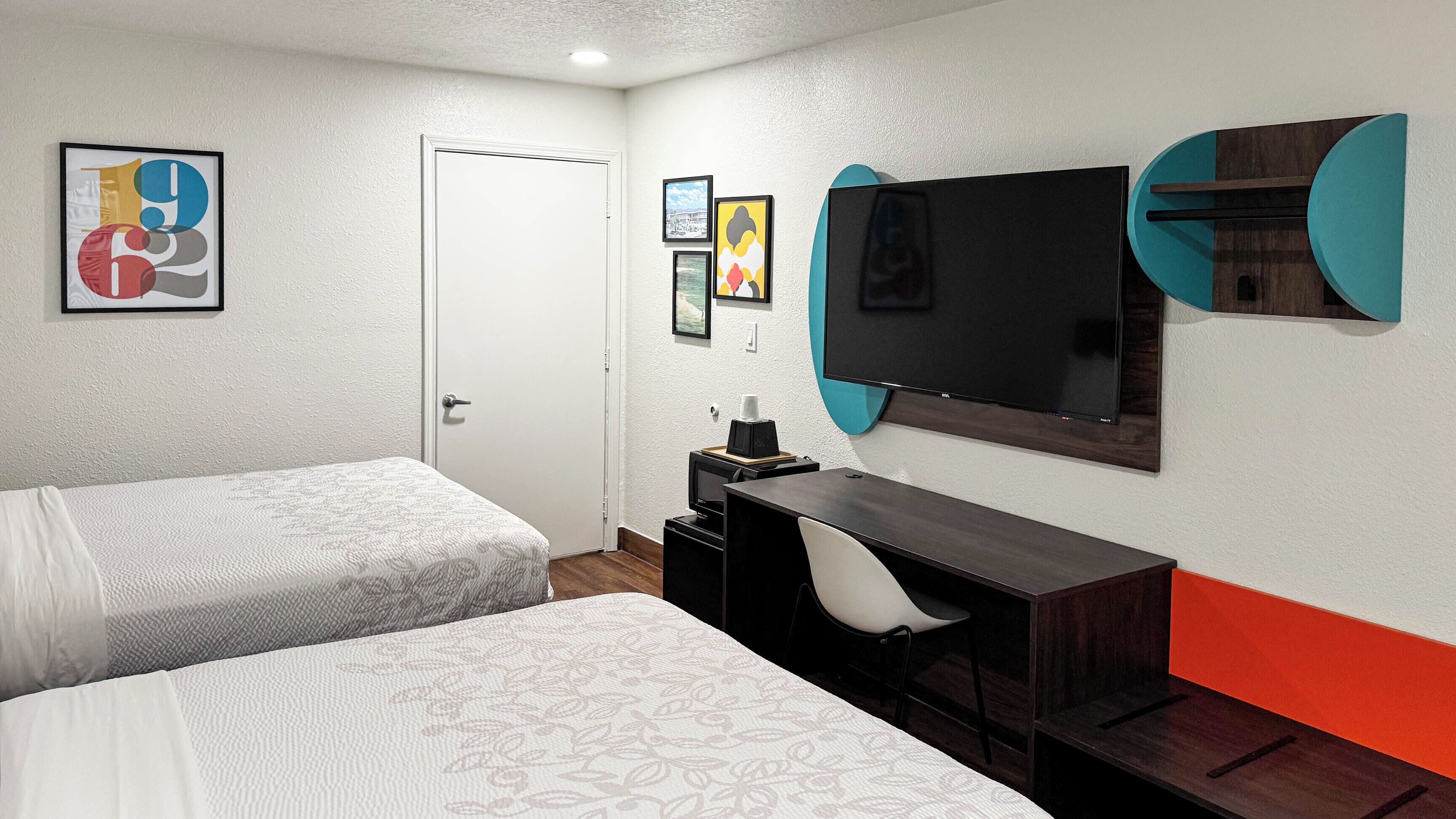 Une chambre d’hôtel avec deux lits, un bureau, une télévision et des œuvres d’art accrochées aux murs.