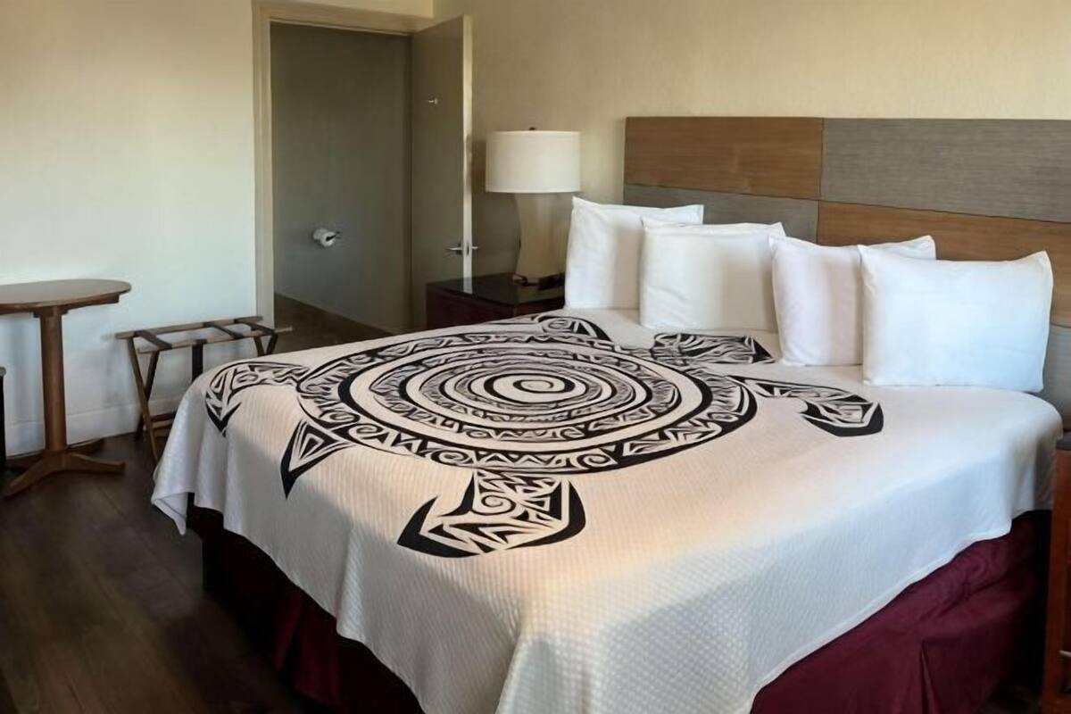 A hotel room with a bed, a bedside table, a lamp, and a door.