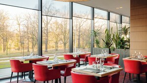 Un restaurante con amplios ventanales, sillas rojas y mesas dispuestas para comer.