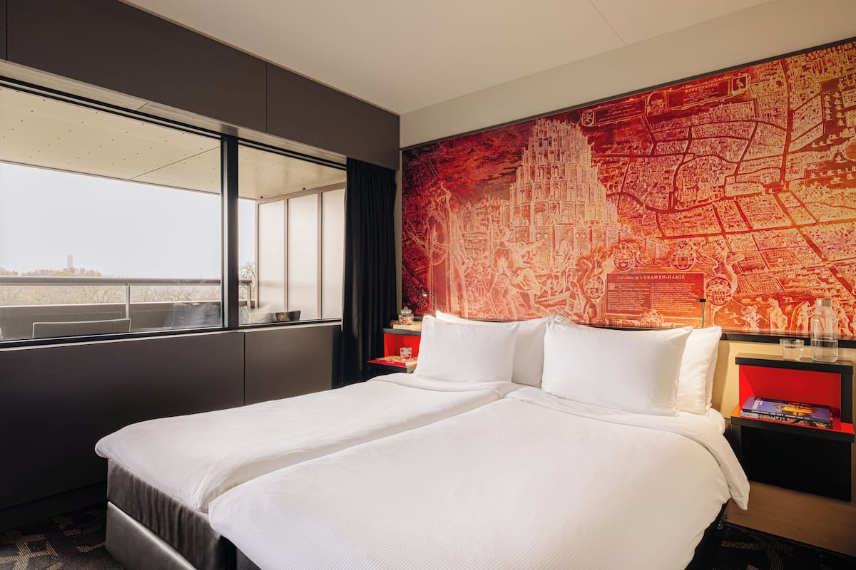 A hotel room with a large bed, a window with a view, and a red map on the wall.