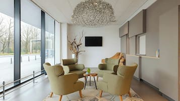 A modern interior with two armchairs, a small table, a decorative vase, and a large window offering a view of the outside.