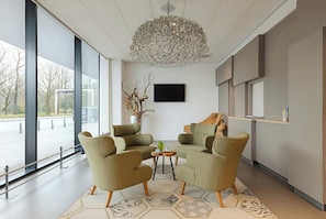 A modern interior with two armchairs, a small table, a decorative vase, and a large window offering a view of the outside. - Leonardo Hotel Den Haag Babylon (The Hague)