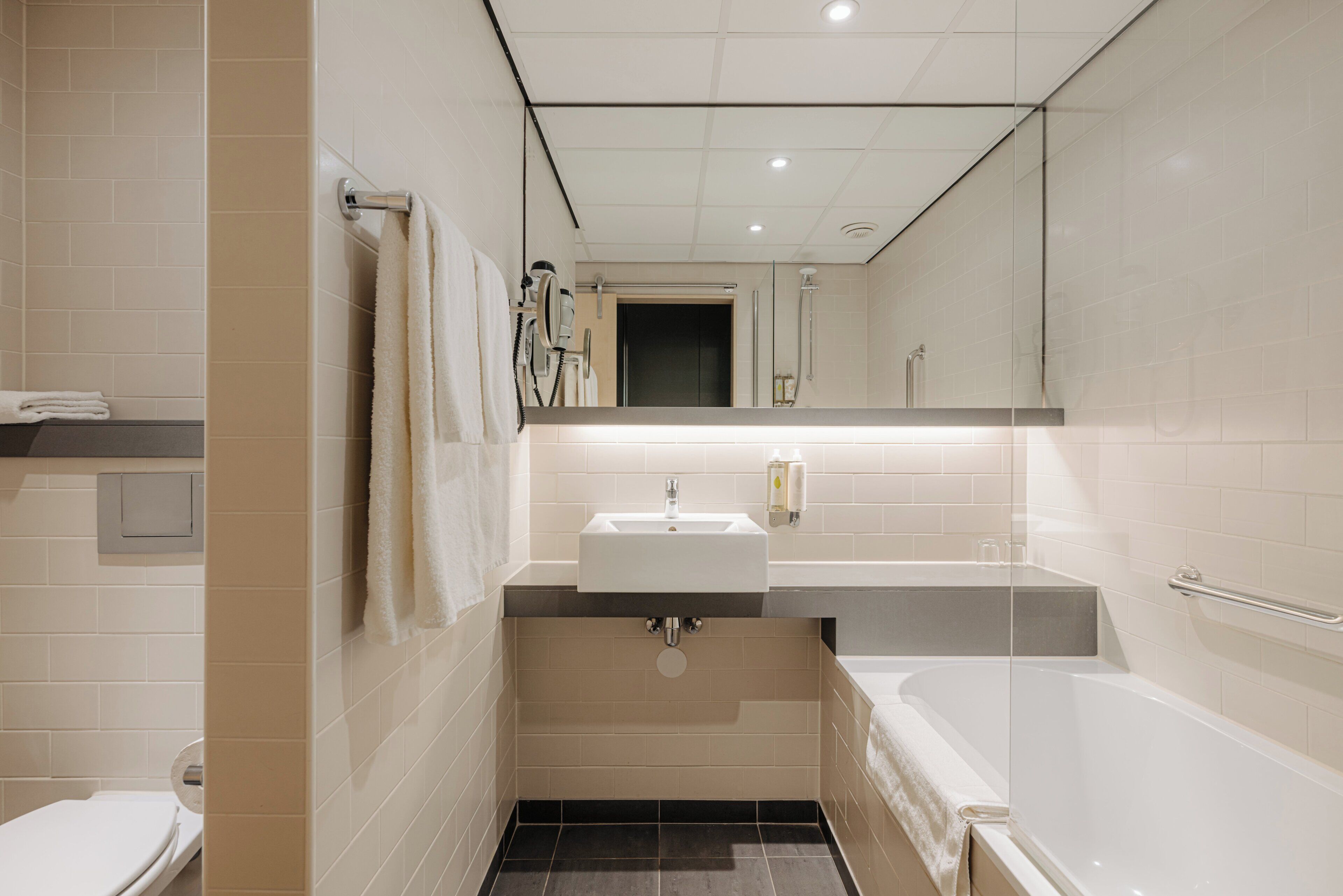 A modern bathroom with a sink, mirror, and bathtub.