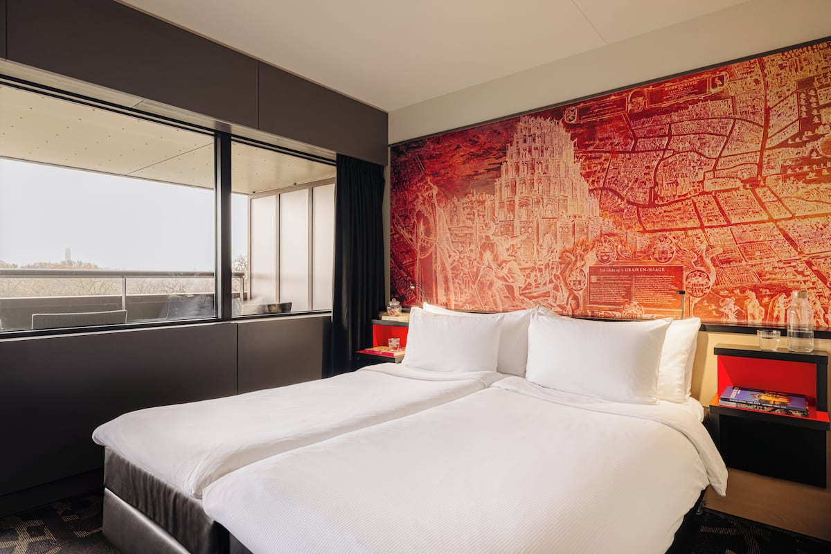 A hotel room with a large bed, a window with a view, and a red map on the wall.