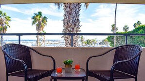 A balcony with two chairs and a small table, overlooking a marina with boats and palm trees. - Beachside Inn (Santa Barbara)