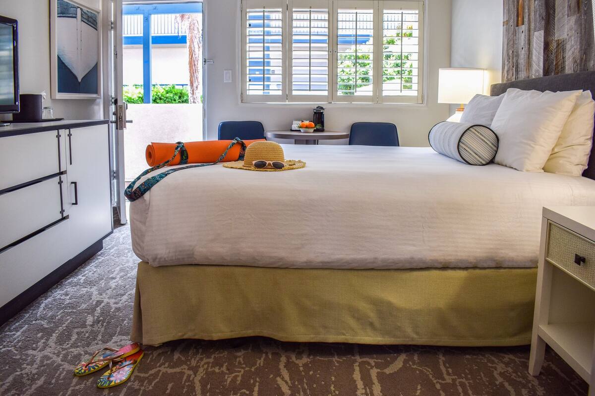 A hotel room with a bed, a desk, a chair, and a window with a view of greenery.
