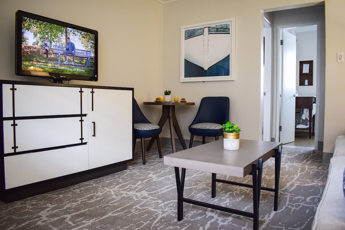 A modern living room with a flat-screen TV, a dining table with two chairs, a sofa, and a small side table with a plant.