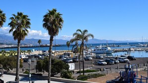 A marina with parked cars and boats, palm trees, and a clear blue sky. - Beachside Inn (Santa Barbara)