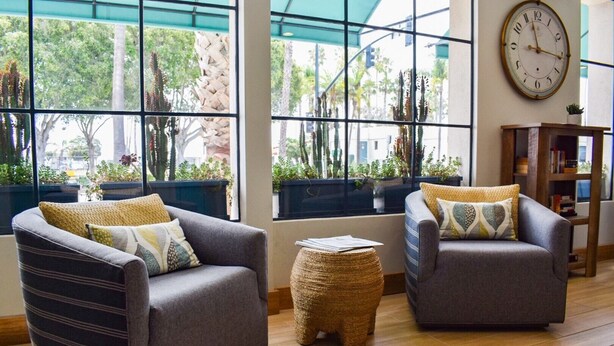 A modern living room with two grey sofas, a small woven stool, and a large wall clock. - Beachside Inn (Santa Barbara)
