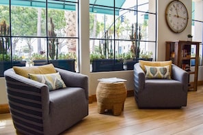 A modern living room with two grey sofas, a small woven stool, and a large wall clock.