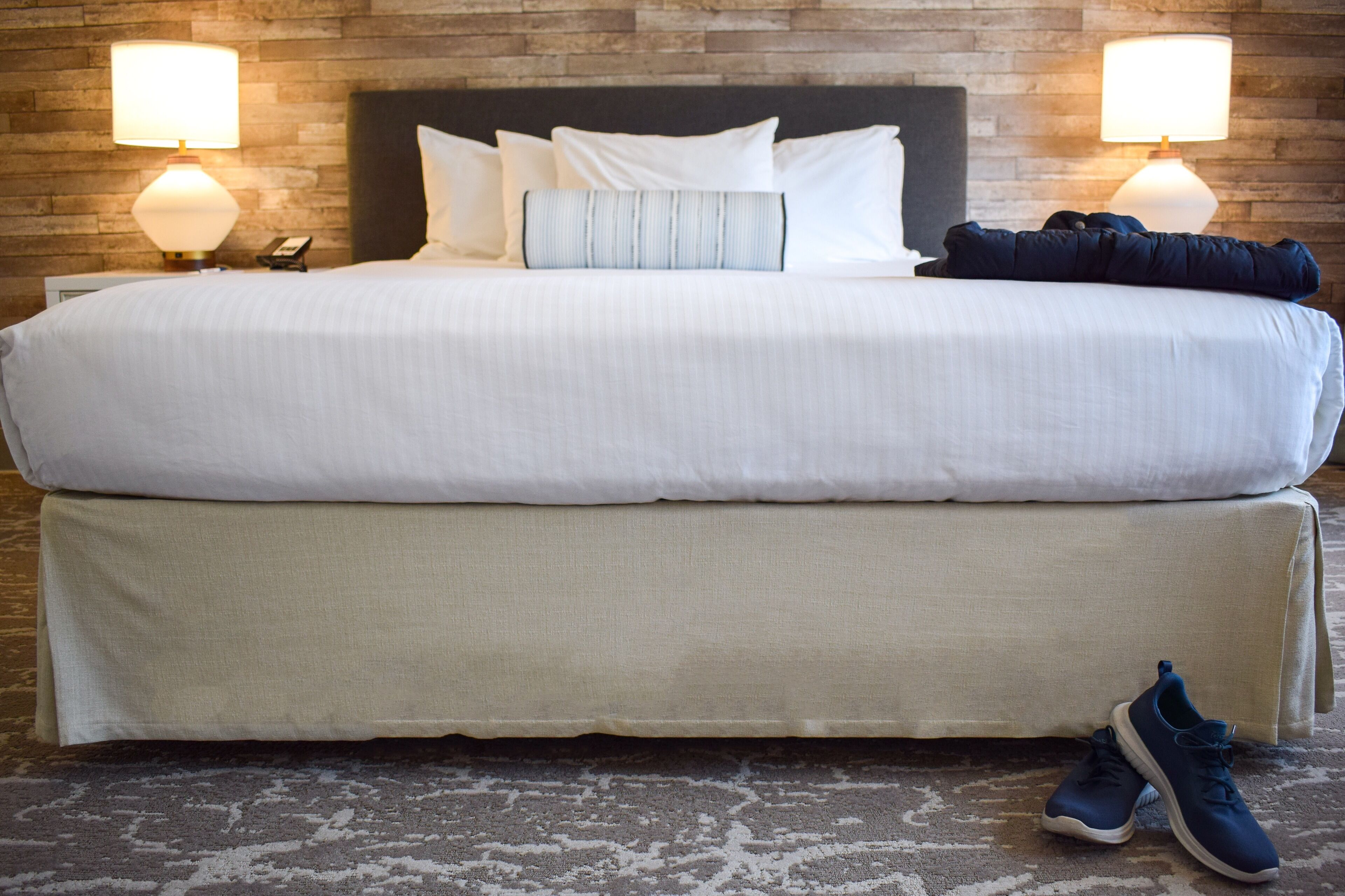 A large bed with white bedding, two bedside lamps, and a pair of shoes on the floor.