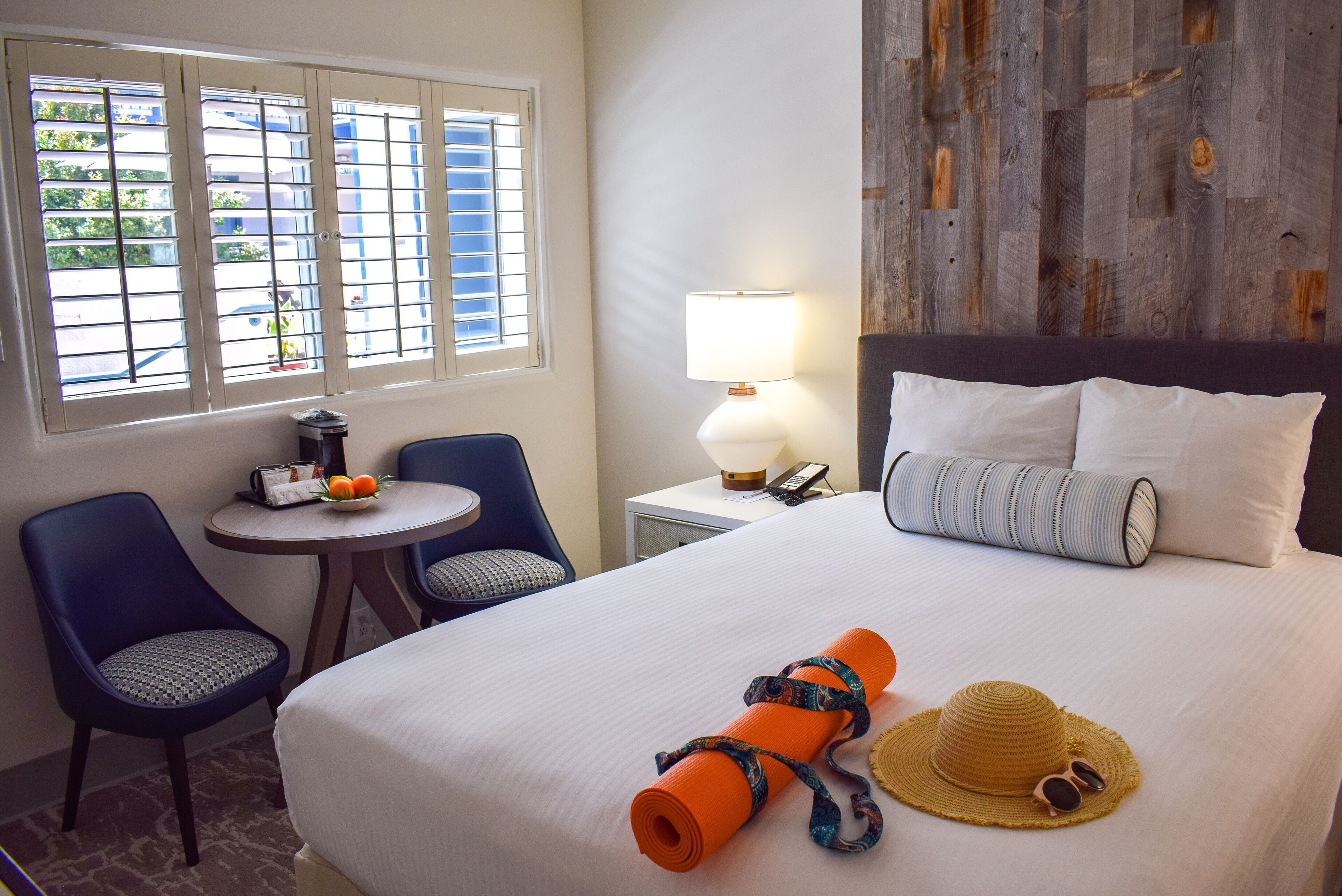 A hotel room with a bed, a desk with a chair, a lamp, and a view of the outside through the window.