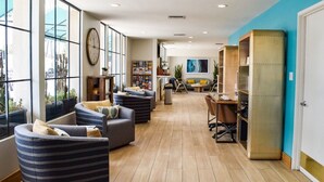 A spacious lobby with large windows, comfortable seating, a reception desk, and a bookshelf. - Beachside Inn (Santa Barbara)