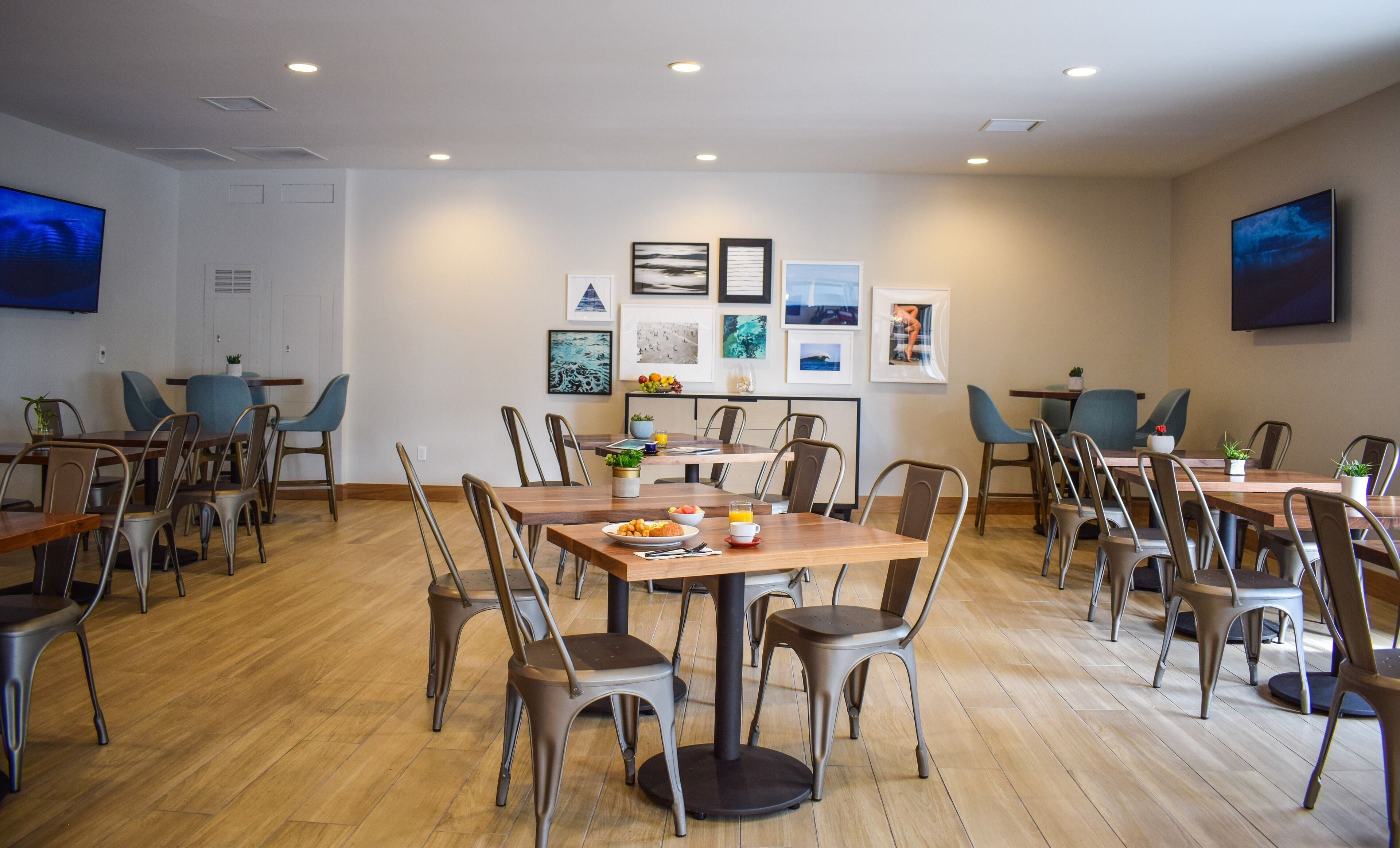 A dining area with multiple tables and chairs, framed artwork on the walls, and a television mounted on the wall.
