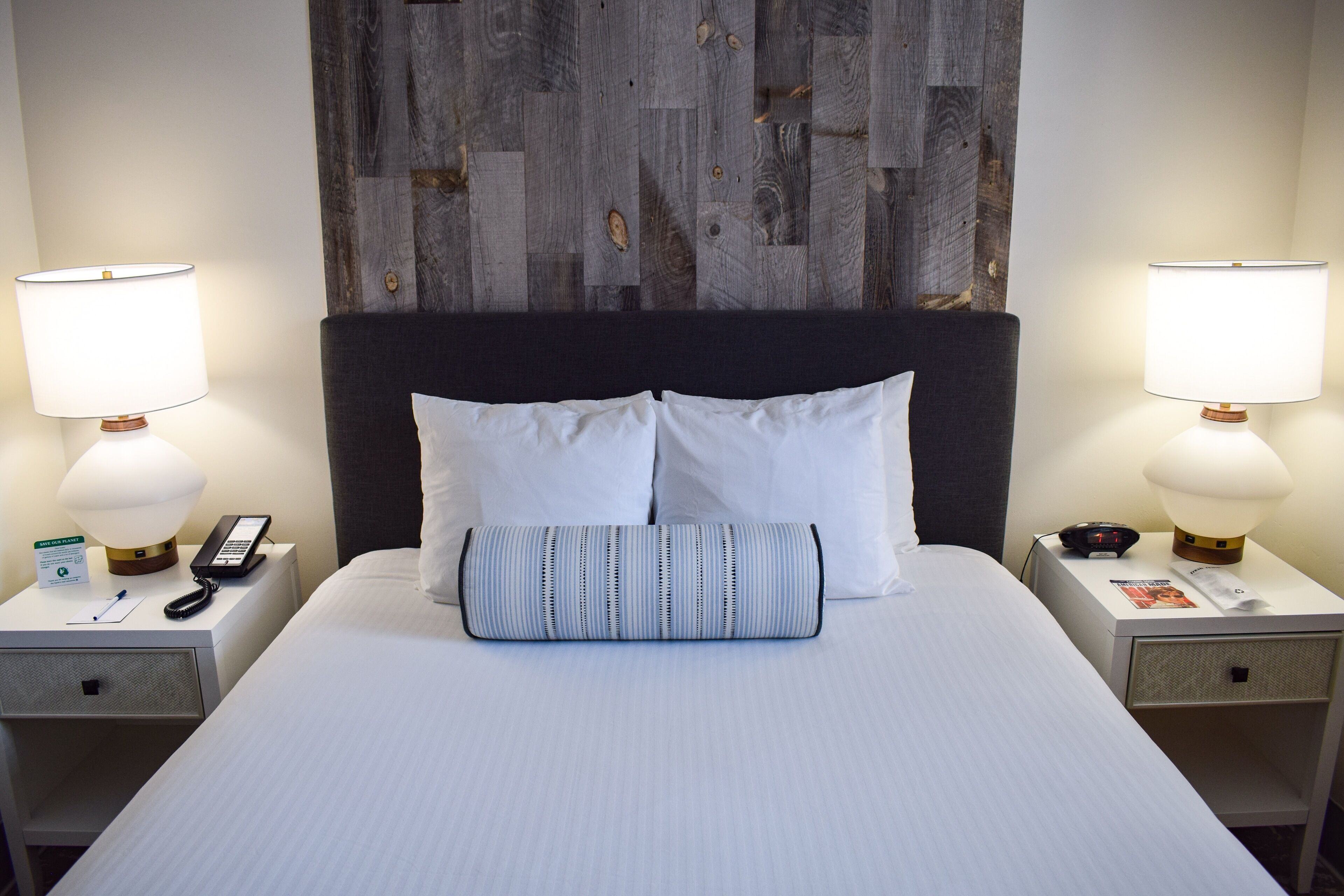 A hotel room with a large bed, two bedside tables, a nightstand, a headboard, and a wall with a wooden panel design.