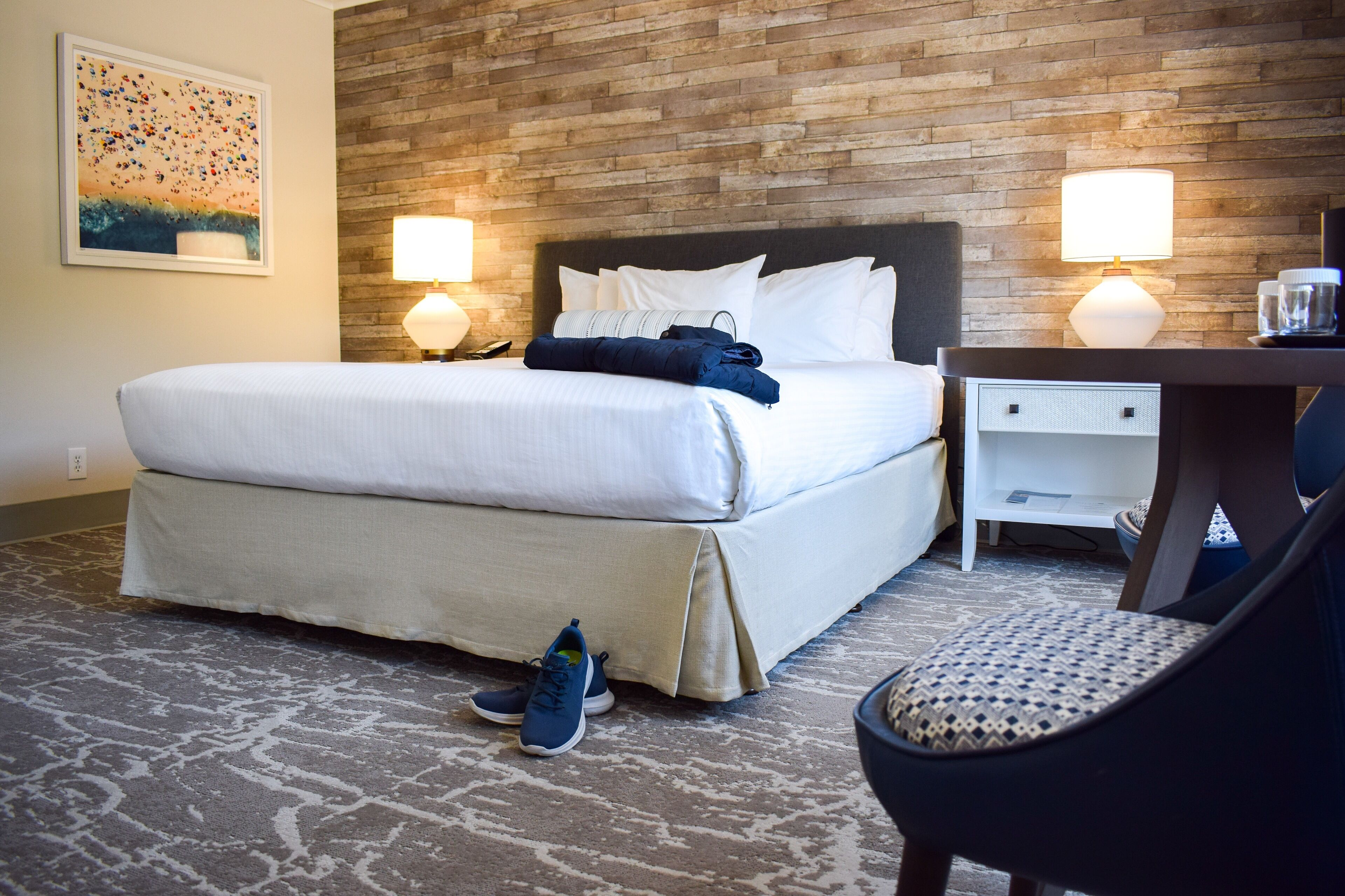 A hotel room with a large bed, two bedside lamps, a desk with a chair, and a patterned rug.
