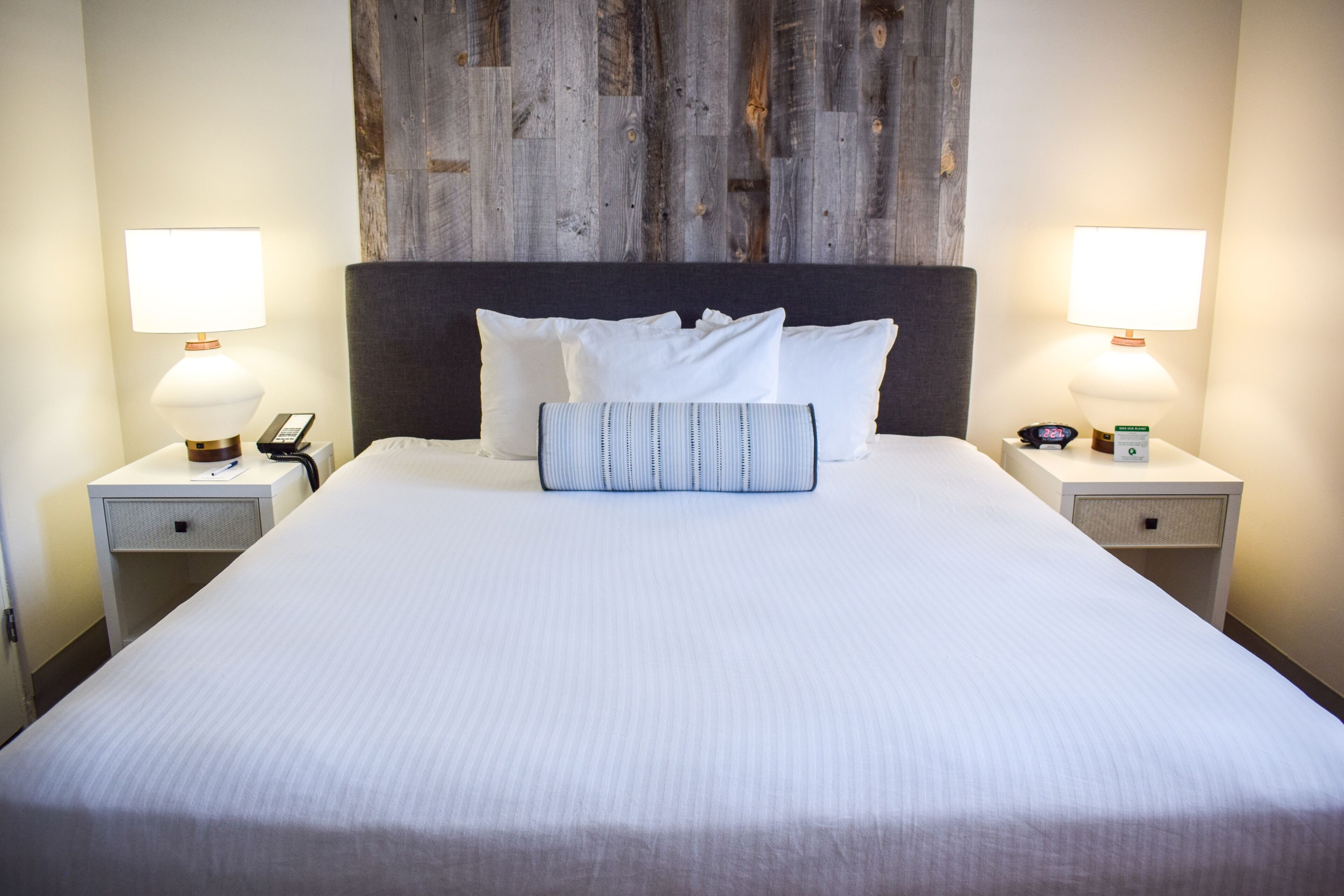 A neatly made bed with white linens, two bedside lamps, and a wooden headboard.