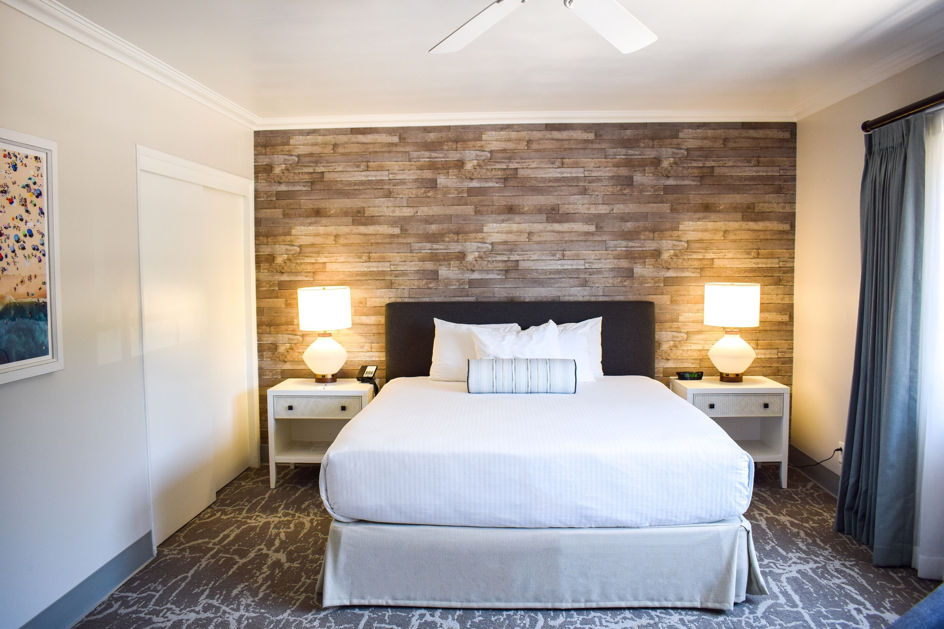 A hotel room with a large bed, two bedside tables with lamps, a wooden accent wall, and a ceiling fan.